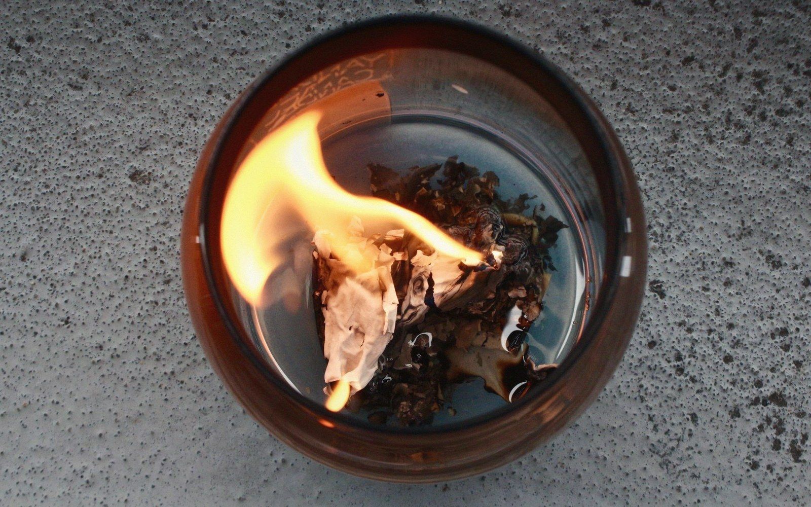 A tea bag burns with an open flame inside a glass candle holder