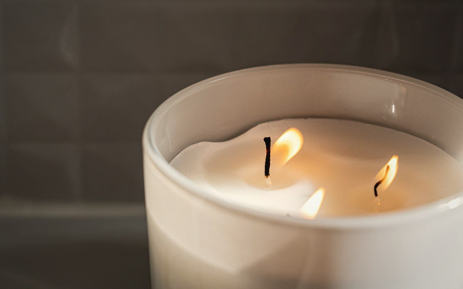 Close-up of a three-wick candle burning in a white glass jar