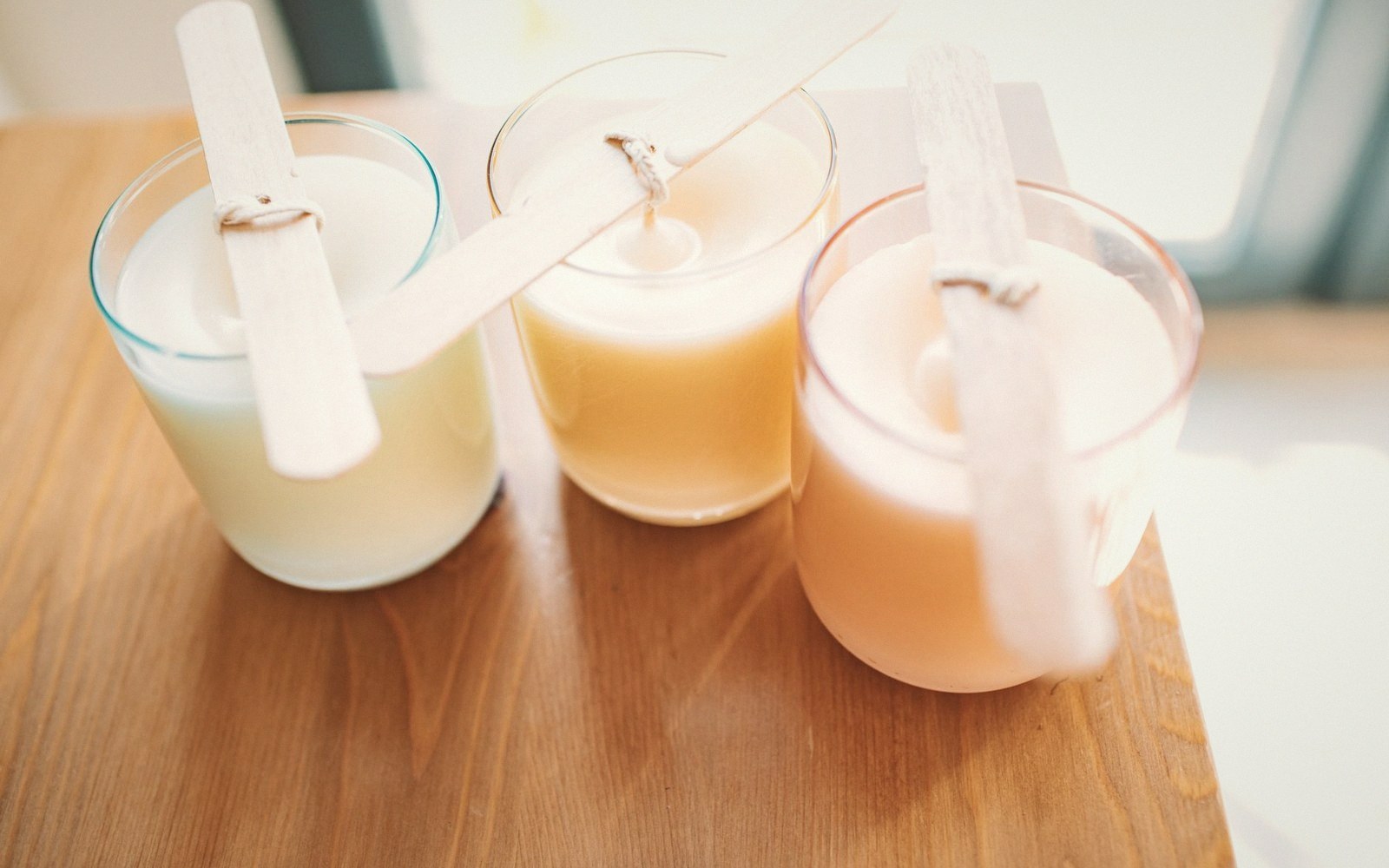 Three glass jar candles cooling with wicks tied to wooden sticks on a table