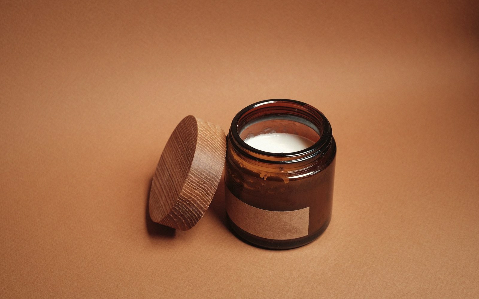 A full melt pool in a wide amber jar, liquid wax touching the container wall at every point, shot from slightly above with a single flame reflection visible in the surface